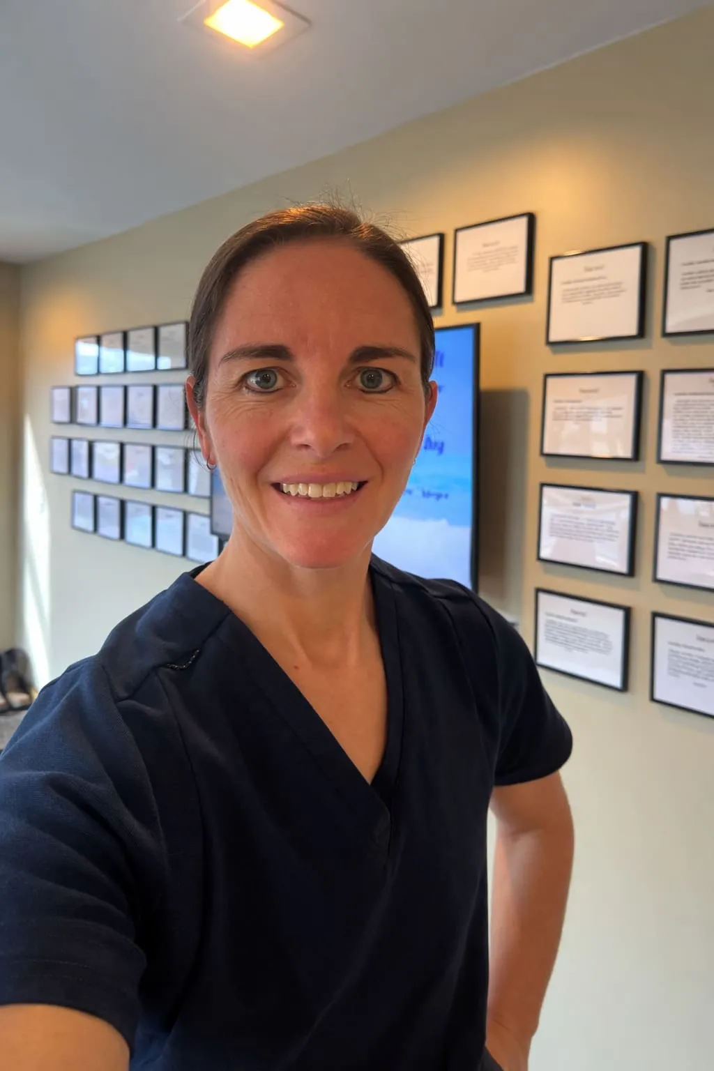 Sarah Vogt smiling in a clinic setting wearing navy medical scrubs