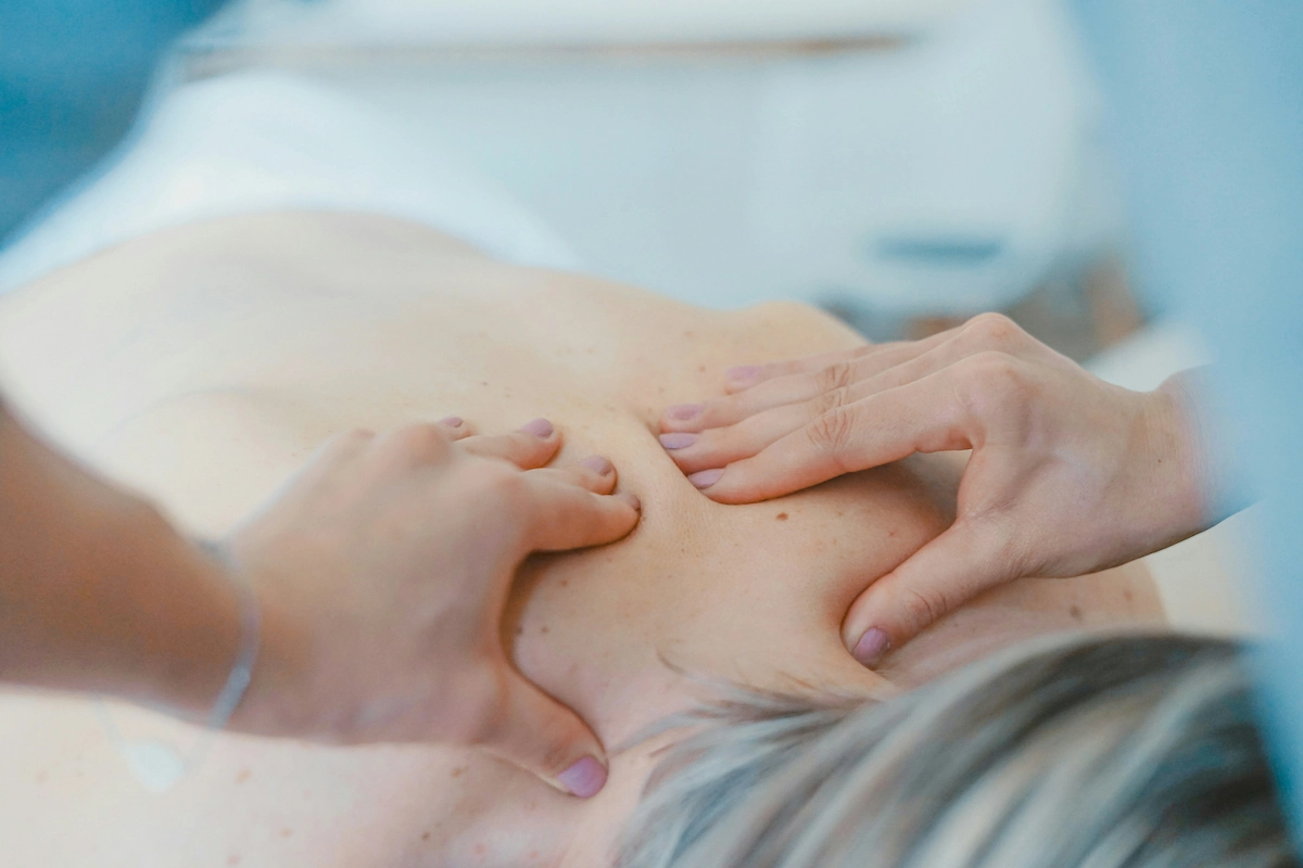 Two hands performing a deep tissue massage on a person's upper back and shoulders.