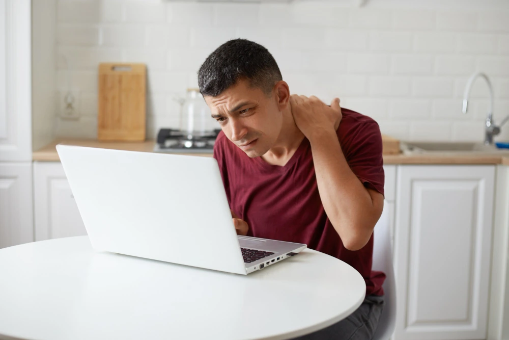Man sitting at desk working on laptop with IT band syndrome pain